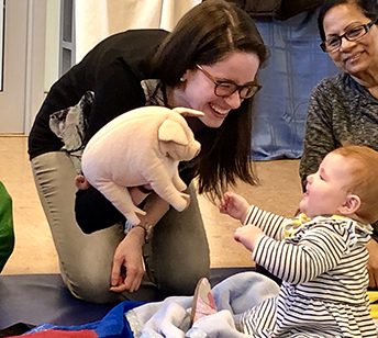 A woman holding a stuffed animal and petting a baby.